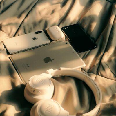 A collection of Apple devices including MacBook, iPad, and iPhone on a bed with sunlight.