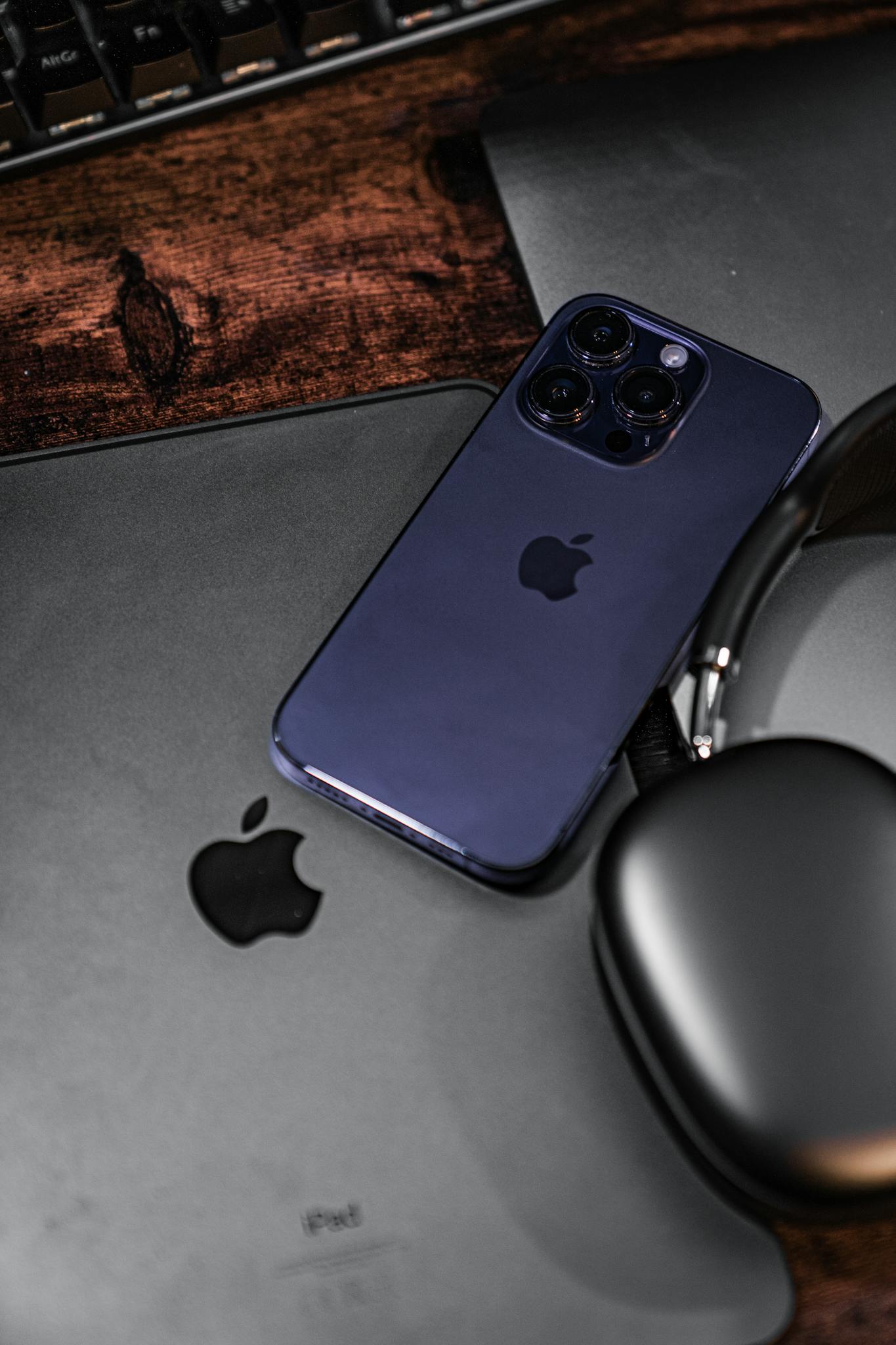 A sleek iPhone, iPad, and headphones on a rustic wooden desk.