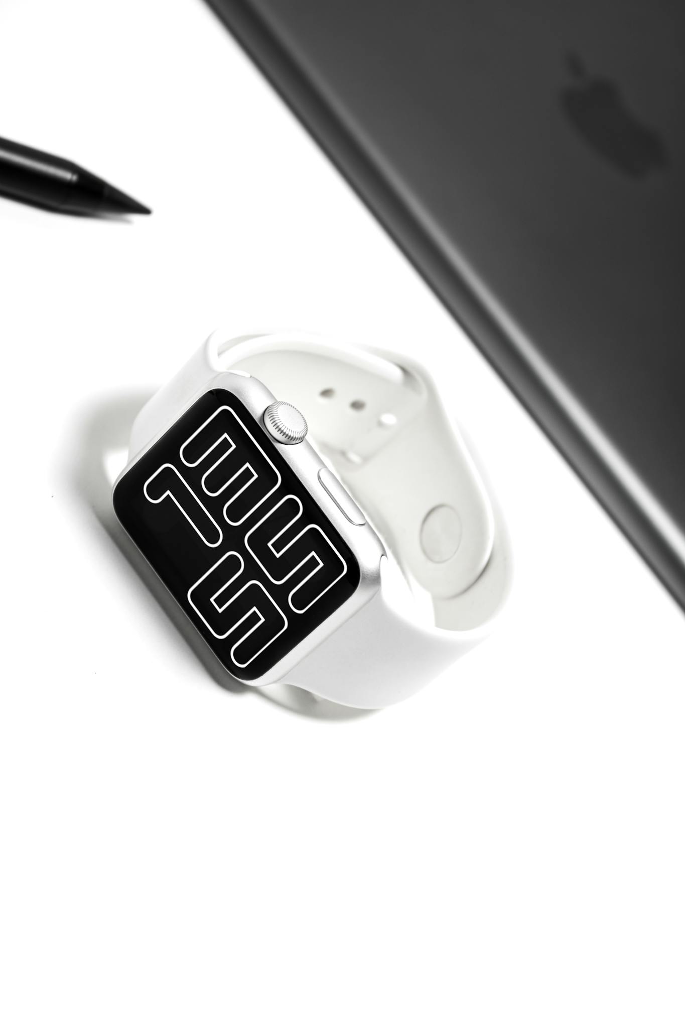 A sleek white smartwatch with a digital display on a minimalist desk setup.