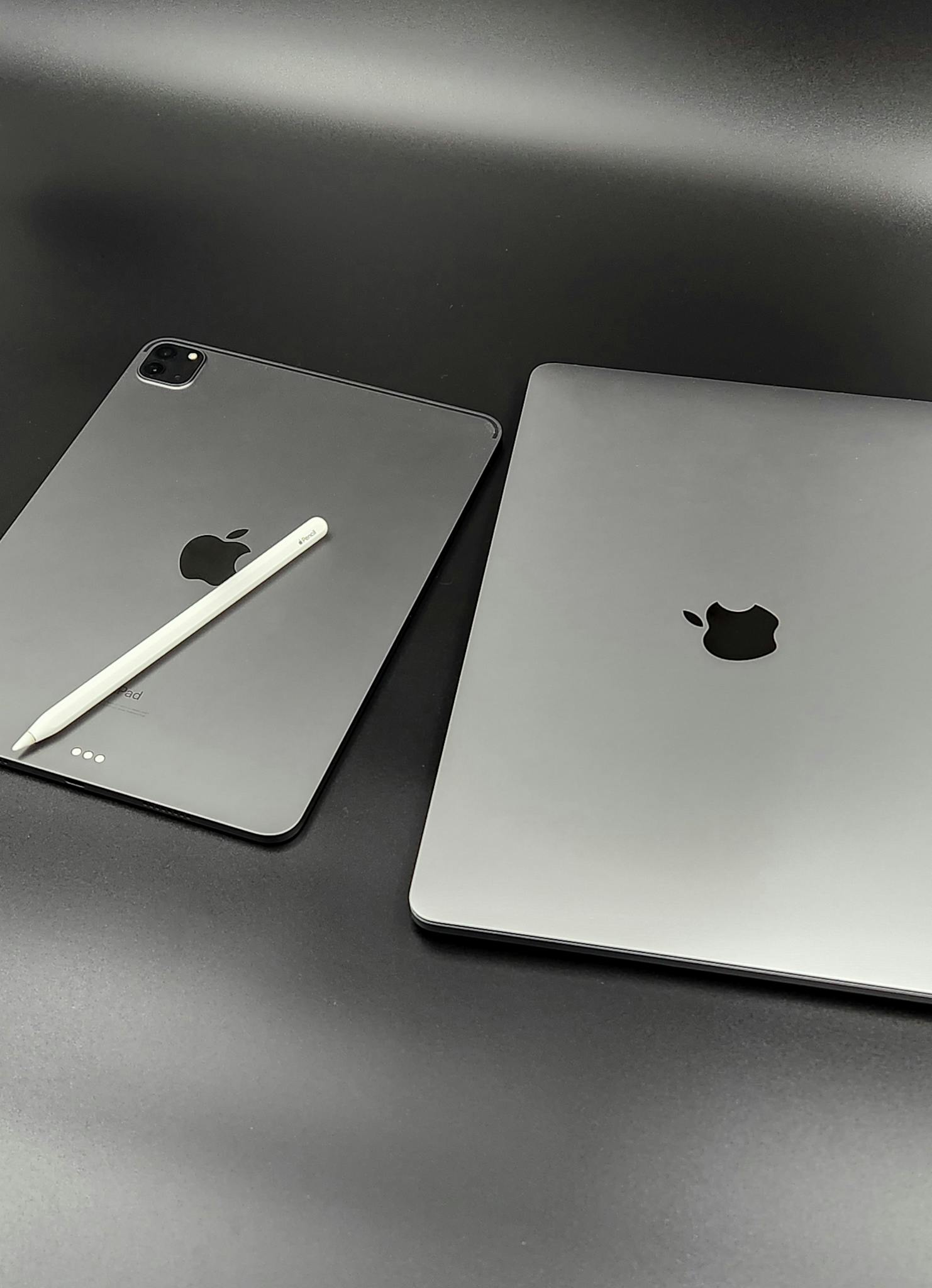 A stylish composition featuring a sleek Apple iPad and MacBook paired with an Apple Pencil on a modern black background.