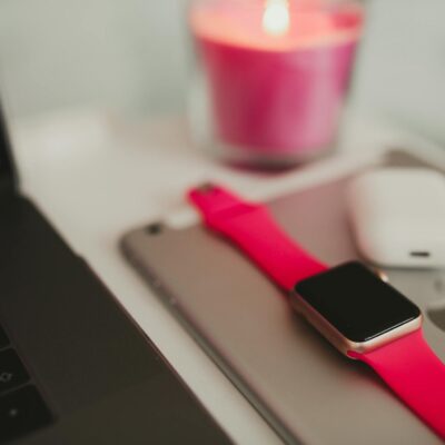 Close-up of laptop, smartwatch, AirPods, and candle set on a table.