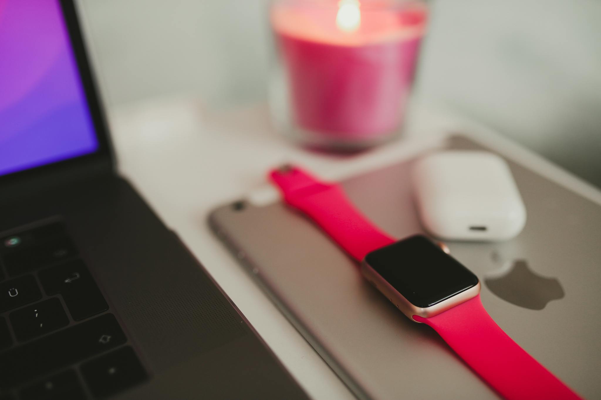 Close-up of laptop, smartwatch, AirPods, and candle set on a table.