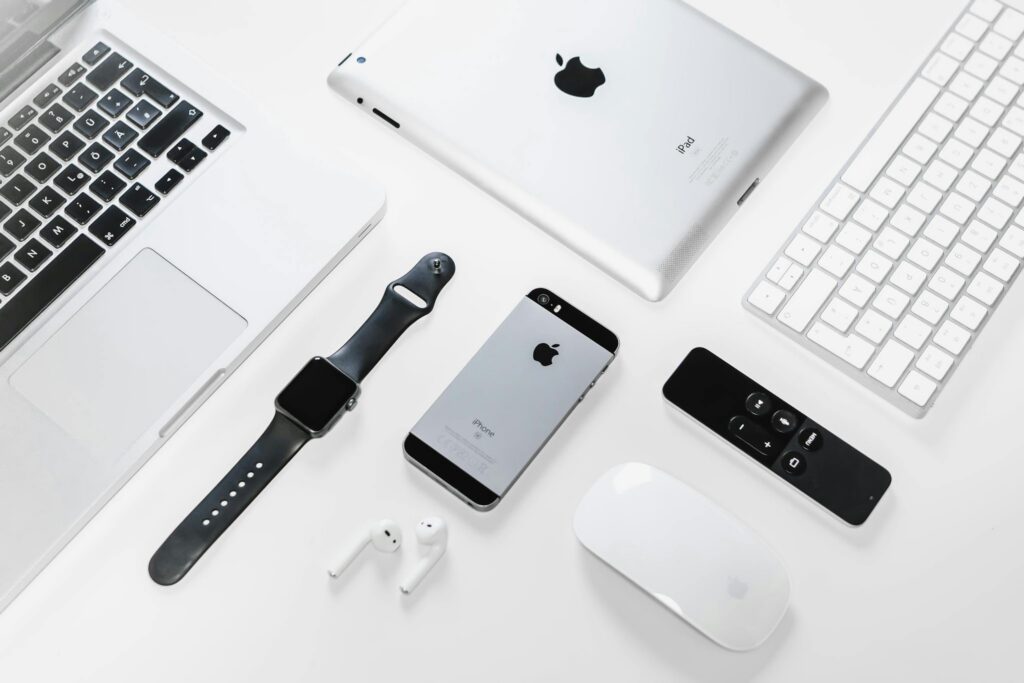 Flat lay of Apple devices including iPhone, iPad, MacBook, and Watch on a white surface, ideal for tech enthusiasts.